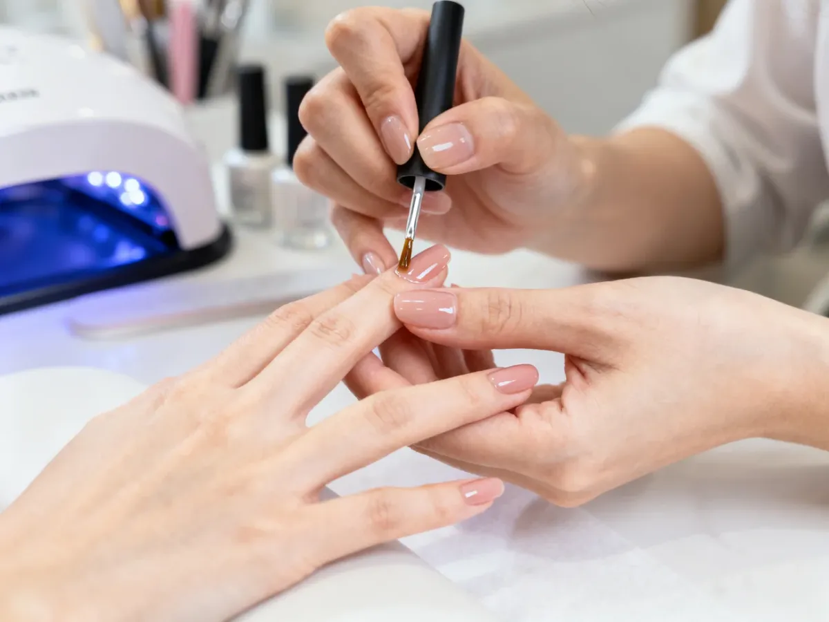 Nakładanie błyszczącego top coatu na paznokcie podczas manicure hybrydowego