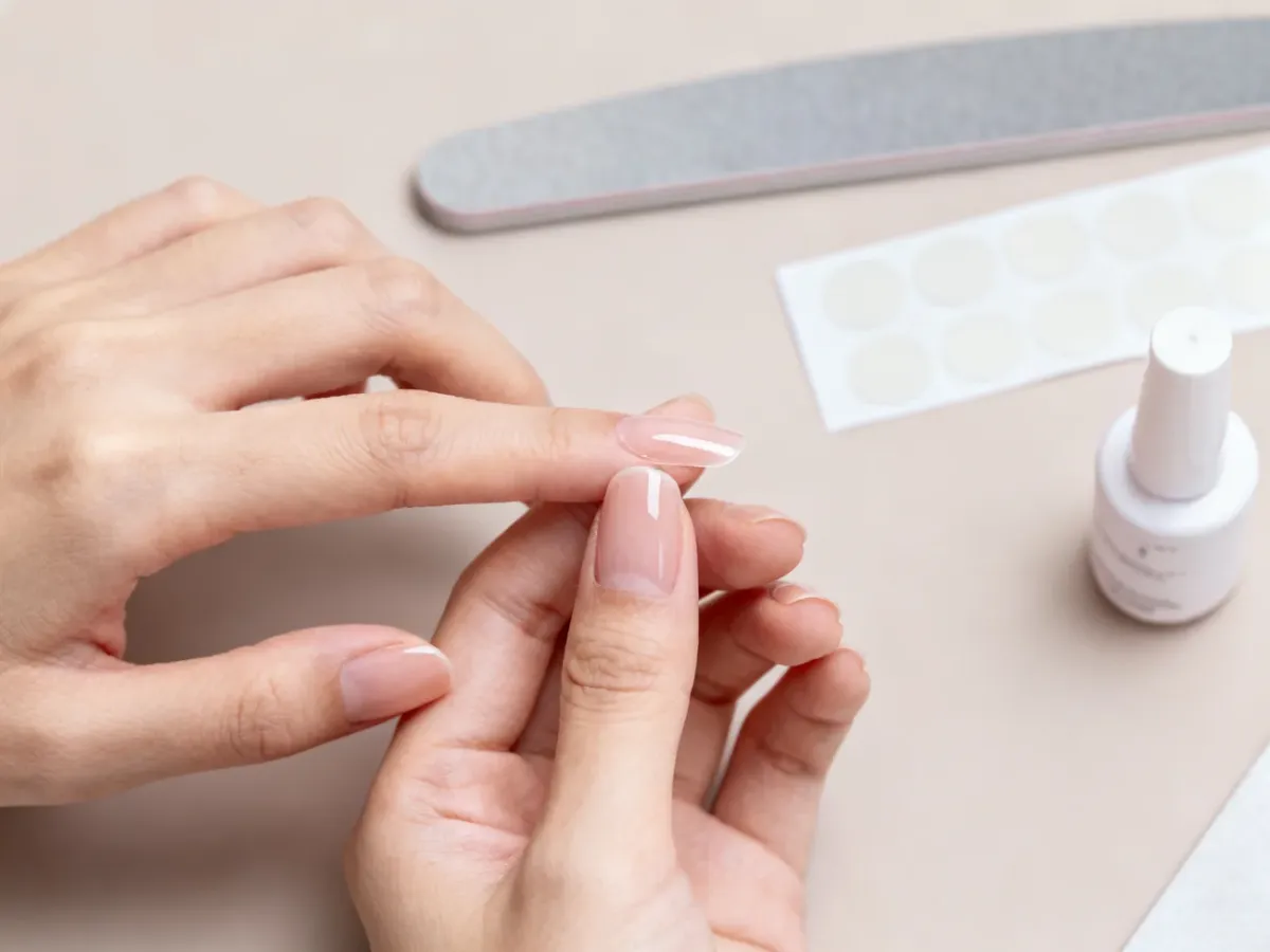A person carefully applying a press-on nail during a home manicure