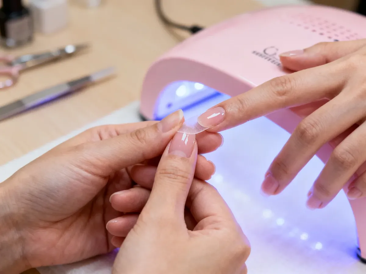 Stylistka nakładająca cienką warstwę żelu na naturalne paznokcie klientki