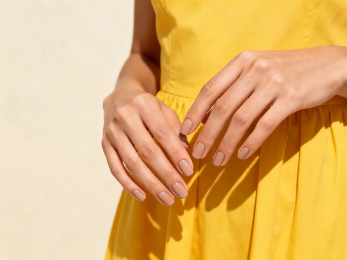Dłoń z eleganckim nude manicure przy żółtej sukience